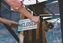 Caucasian female turning sign from open to closed on the entrance door of his small cafe. Out of business