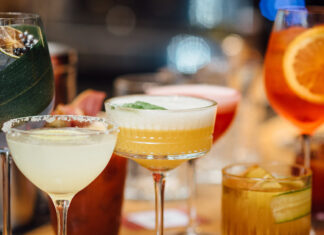 10 Beverage Trends for 2026 Сolorful cocktails close-up in elegant glassware, garnished with fruits and herbs, captured with a shallow depth of field for bokeh effect. Bright indoor bar setting with blurred background, vertical image