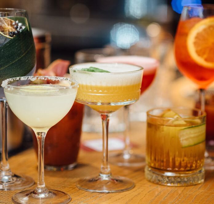 Сolorful cocktails close-up in elegant glassware, garnished with fruits and herbs, captured with a shallow depth of field for bokeh effect. Bright indoor bar setting with blurred background, vertical image