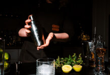 Woman bartender shaking cocktail in metal shaker with two hands. Intensive mixing process for refreshing drink and nightlife entertainment concept.