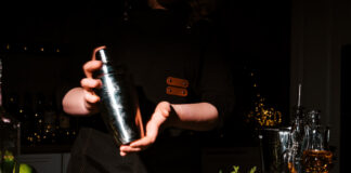 Woman bartender shaking cocktail in metal shaker with two hands. Intensive mixing process for refreshing drink and nightlife entertainment concept.